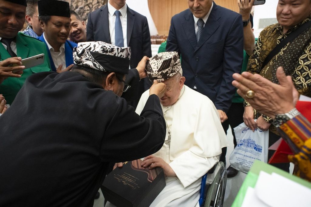 RD Fadjar Tedjo Soekarno Imam dari Keuskupan Malang memasangkan udeng Osing, Banyuwangi, kepada Paus Fransiskus di Vatikan, Rabu (21/8/2024). Udeng Banyuwangi memiliki kekhasan bentuk segitiga di sisi kiri dan kanan. Segitiga itu mewakili nilai-nilai keselarasan.