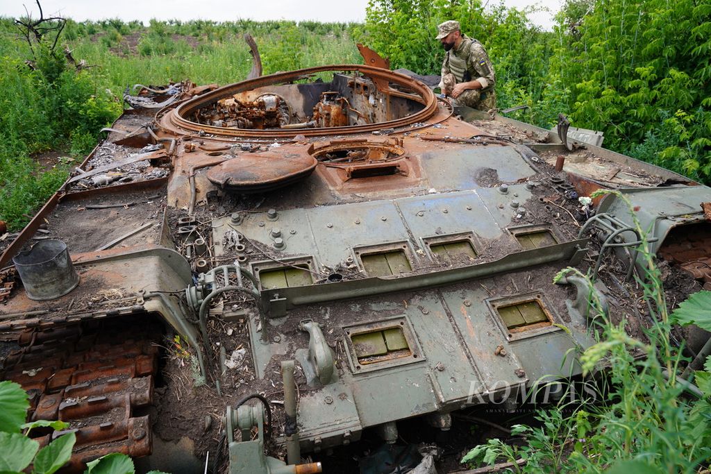 Anggota militer Ukraina memeriksa bagian tank milik Rusia yang hancur di sebuah ladang pertanian di Desa Mala Rohan, Provinsi Kharkiv, Ukraina, Selasa (5/7/2022). Banyak bahan peledak ataupun ranjau yang belum dijinakkan terserak di ladang pertanian di Ukraina. 