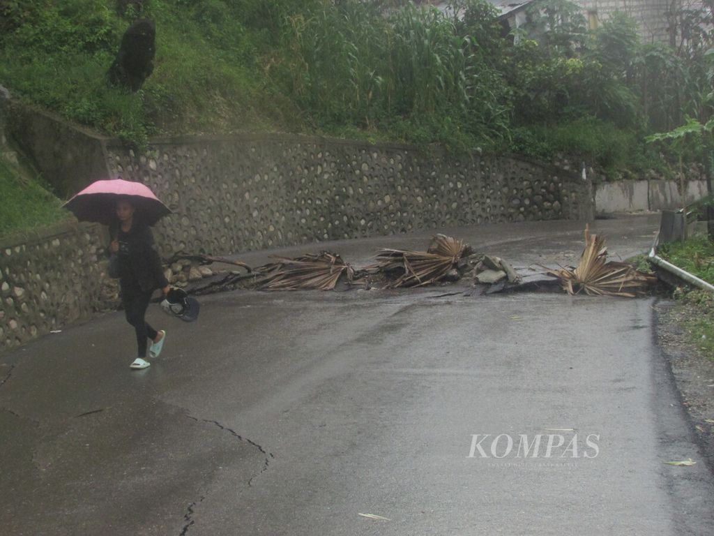 Trince (25), warga Kelurahan Liliba, Kota Kupang, berjalan kaki menuju tempat kerja setelah ruas Jalan Taebenu di Kota Kupang putus, Kamis (14/3/2024).