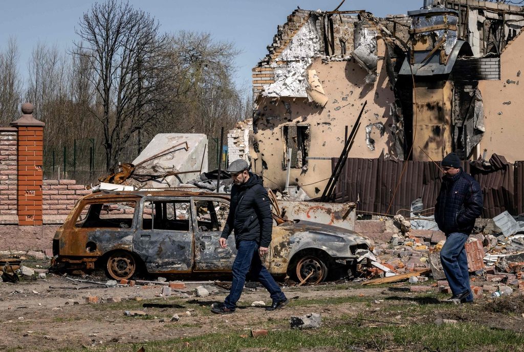 Dua pria berjalan melewati mobil yang terbakar dan bangunan yang hancur di Desa Bohdanivka, dekat Kyiv, Ukraina, 14 April 2022, di tengah invasi Rusia. 