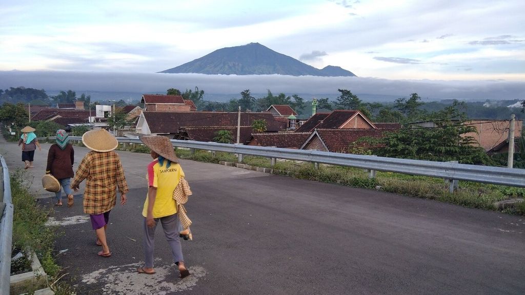 Beberapa buruh tani berjalan menyusuri jalan di Desa Watu Gede, Kecamatan Singosari, Kabupaten Malang, Jawa Timur, di suatu pagi di awal Desember 2020. Tampak di belakang Gunung Arjuno yang sebagian badannya masih terselimuti kabut.