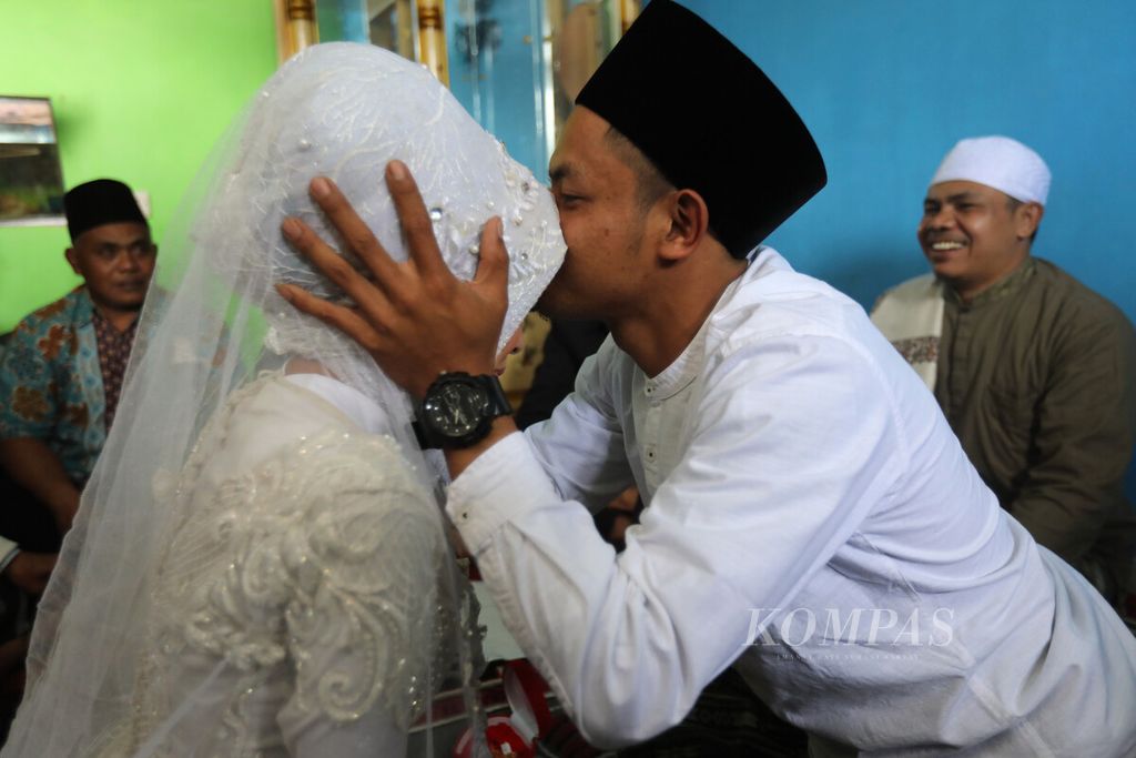 Mempelai laki-laki, Muhammad Nurdin (kanan), mencium dahi istrinya, Nida Khovia Syukur, setelah melaksanakan akad nikah di kediaman mempelai perempuan di Kampung Kuta Wetan, Desa Mangunkerta, Kecamatan Cugenang, Kabupaten Cianjur, Jawa Barat, Minggu (4/12/2022).