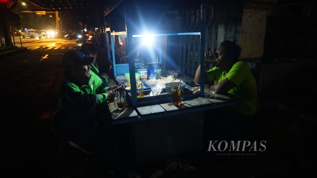 Para pengemudi ojek daring menikmati wedang dan makanan di sebuah hik di Jalan Slamet Riyadi, Kota Surakarta, Jawa Tengah, Selasa (23/3/2022). Hik bukan sekadar tempat jajan. Tempat itu sekaligus menjadi ruang interaksi sosial bagi warga untuk mencurahkan keresahannya tentang berbagai hal.