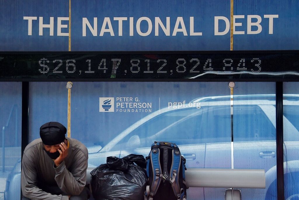 Seorang pria menanti di halte bus yang memajang papan reklame bertuliskan besaran utang nasional Amerika Serikat di Washington DC, 19 Juni 2020. 
