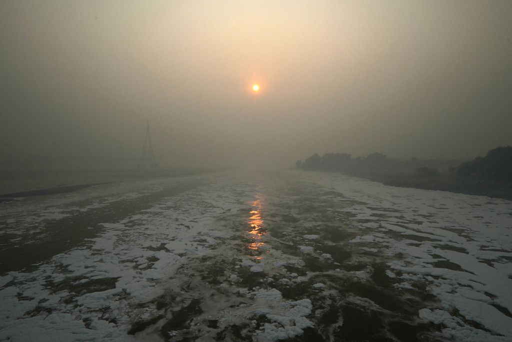 Matahari terbit di langit yang pekat oleh polusi udara di atas sungai berbusa oleh polusi di New Delhi, India, 13 November 2023.