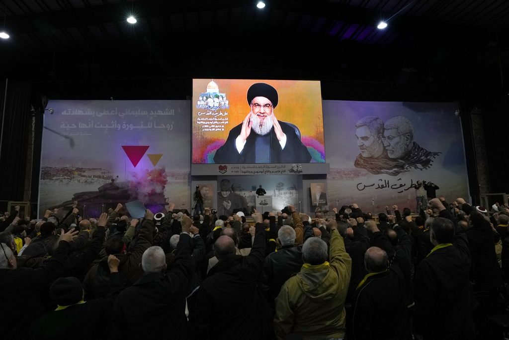 Pemimpin Hezbollah, Sayyed Hassan Nasrallah (tampak di layar), menyapa pendukungnya melalui siaran di pinggiran selatan kota Beirut, Lebanon, dalam peringatan empat tahun kematian Komandan Brigade Al-Quds Garda Revolusi Iran Qassem Soleimani, Rabu (3/1/2024).