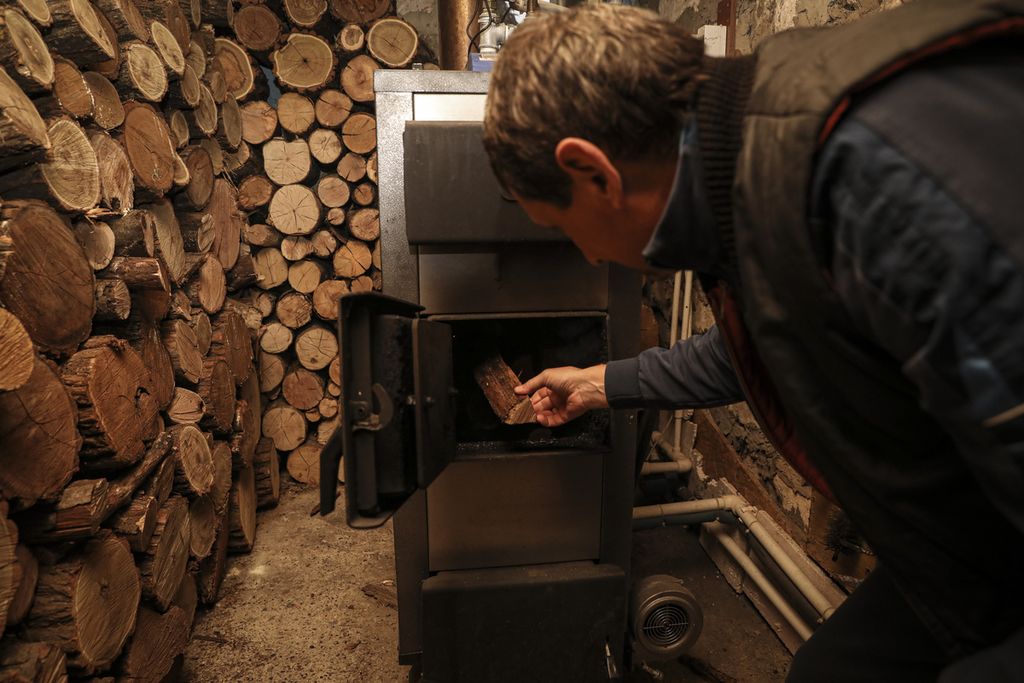 Tudor Popescu memasukkan kayu bakar ke dalam tungku pemanas di ruang bawah tanah di rumahnya yang terletak di Chisinau, ibu kota Moldova, Sabtu (15/10/2022). Popescu mengganti gas sebagai sumber energi dengan kayu bakar setelah harga gas naik hingga enam kali lipat. 