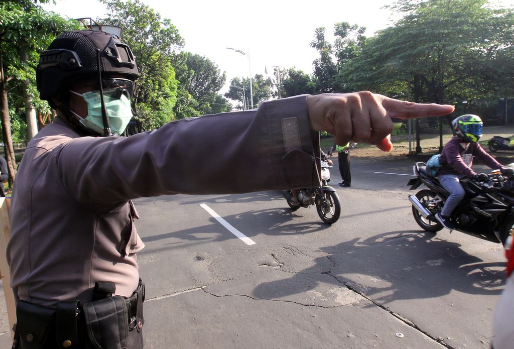 Petugas kepolisian memeriksa pemakaian masker dan identitas pengendara sepeda motor berpenumpang yang melintas di perbatasan Jakarta-Depok, Depok, Jawa Barat, Rabu (15/4/2020), saat PSBB mulai diberlakukannya hari ini. 