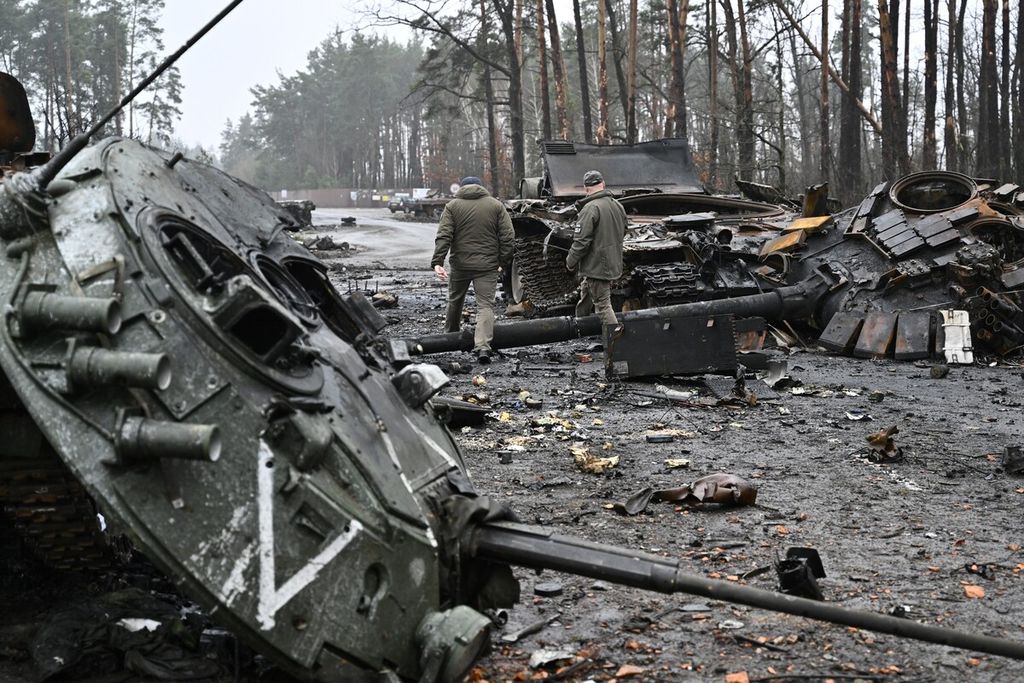 Anggota militer Ukraina melewati sejumlah kendaraan tempur dan tank milik Rusia yang rusak di Desa Dmytrivka, barat Ibu Kota Ukraina, Kiev, Jumat (2/4). (Photo by Genya SAVILOV / AFP)