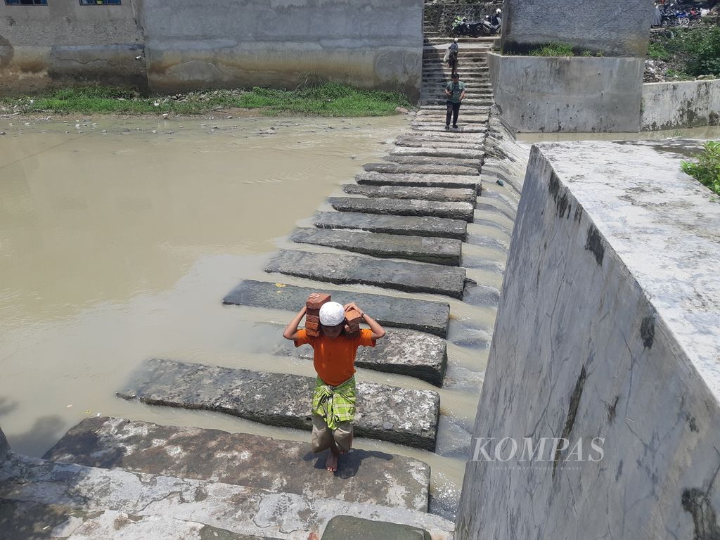 Warga melintasi sungai di Benda Kerep, Kelurahan Argasunya, Kecamatan Harjamukti, Kota Cirebon, Jawa Barat, Senin (12/2/2024). Sepeda motor dan mobil tidak bisa masuk ke kawasan itu karena tidak ada jembatan.
