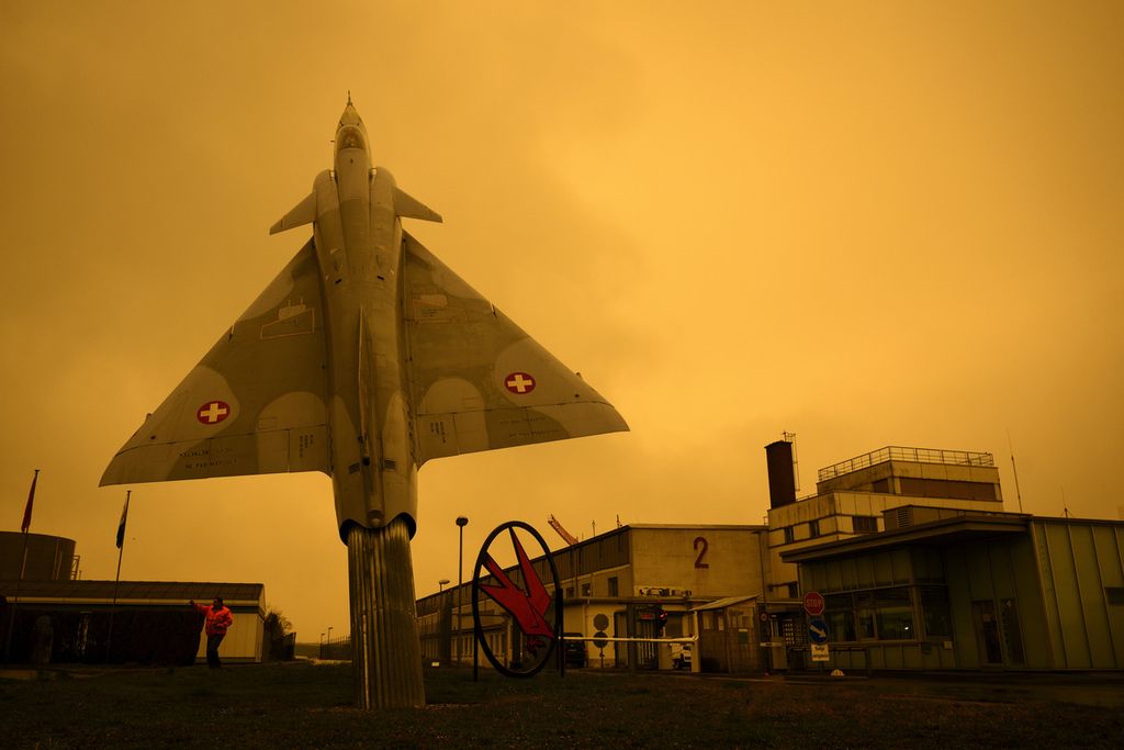 Sebuah pesawat jet tempur bekas milik Angkatan Udara Swiss, Mirage 2000, dipasang di depan pintu gerbang Angkatan Bersenjata Swiss di Pangkalan Udara Payerne saat debu Gurun Sahara mewarnai langit dengan cahaya kuning kemerahan, Selasa (15/3/2022). 