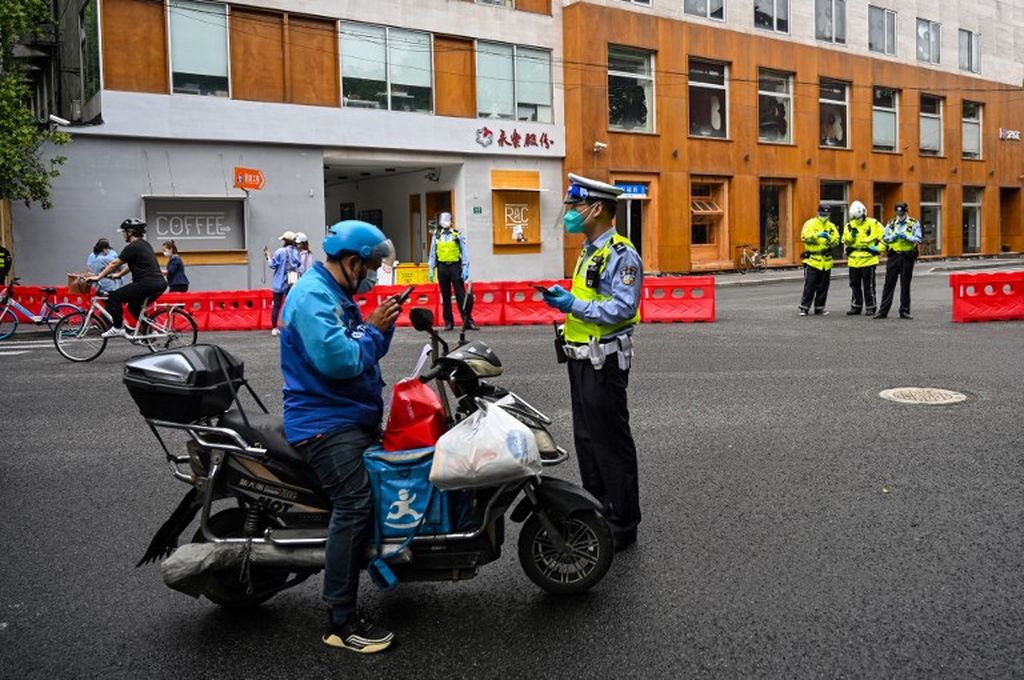 Seorang petugas kepolisian memeriksa seorang kurir barang di sebuah ruas jalan selama penguncian Covid-19 di distrik Xuhui, Shanghai, Minggu (29/5/2022).