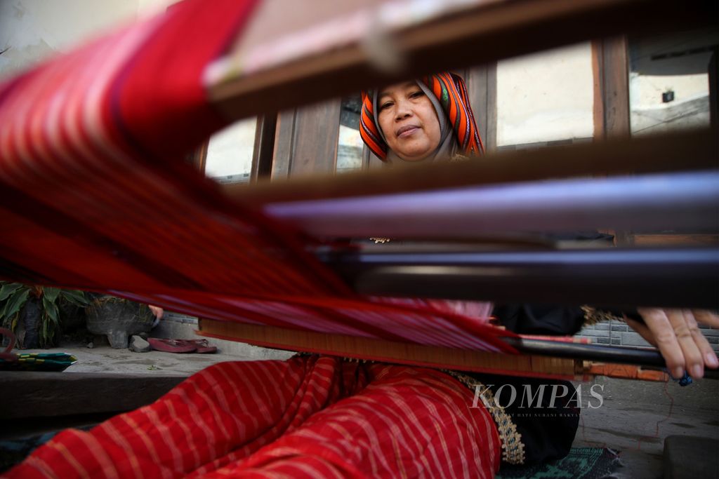Seorang ibu menenun di halaman rumah di Desa Pringgasela Selatan, Kecamatan Pringgasela, Kabupaten Lombok Timur, Nusa Tenggara Barat, Selasa (19/12/2023). Ada sekitar 700 penenun, sebagian besar ibu-ibu, di Pringgasela Selatan. Tidak hanya menjadi penopang ekonomi, tenun bagi masyarakat Pringgasela Selatan juga menjadi pegangan hidup yang diwariskan turun-temurun dan dijaga bersama. 