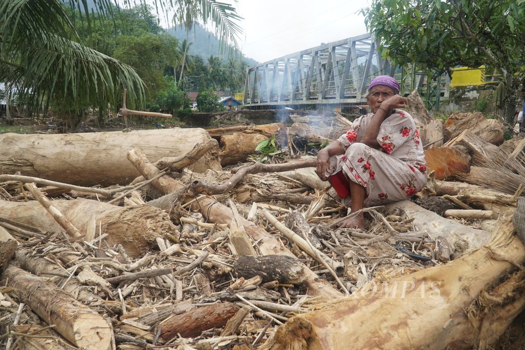 Seorang warga duduk di antara kayu-kayu yang terbawa oleh banjir bandang di Kampung Batu Bala, Nagari Ganting Mudiak Utara Surantih, Kecamatan Sutera, Kabupaten Pesisir Selatan, Sumatera Barat, Kamis (14/3/2024). 