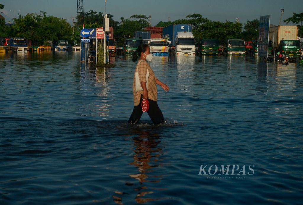 Warga melintasi truk yang terendam banjir pasang air laut di Pelabuhan Tanjung Emas, Kota Semarang, Jawa Tengah, Selasa (24/5/2022). 