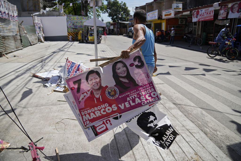 Seorang pekerja desa membersihkan poster kampanye kandidat presiden Ferdinand ”Bongbong” Marcos Jr. (kiri) di sepanjang jalan di kota Quezon, Filipina, Rabu (11/5/2022). 