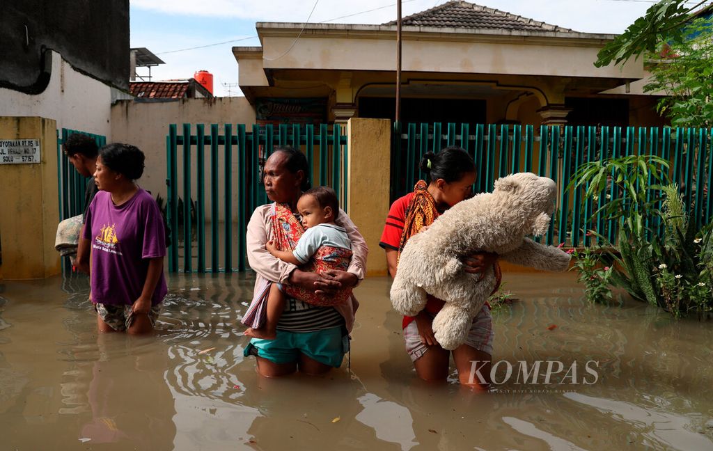 Warga menggendong anak balita saat menunggu petugas untuk membantu evakuasi dari rumahnya yang terendam banjir di Kelurahan Joyotakan, Kecamatan Serengan, Kota Surakarta, Jawa Tengah, Jumat (17/2/2023). 