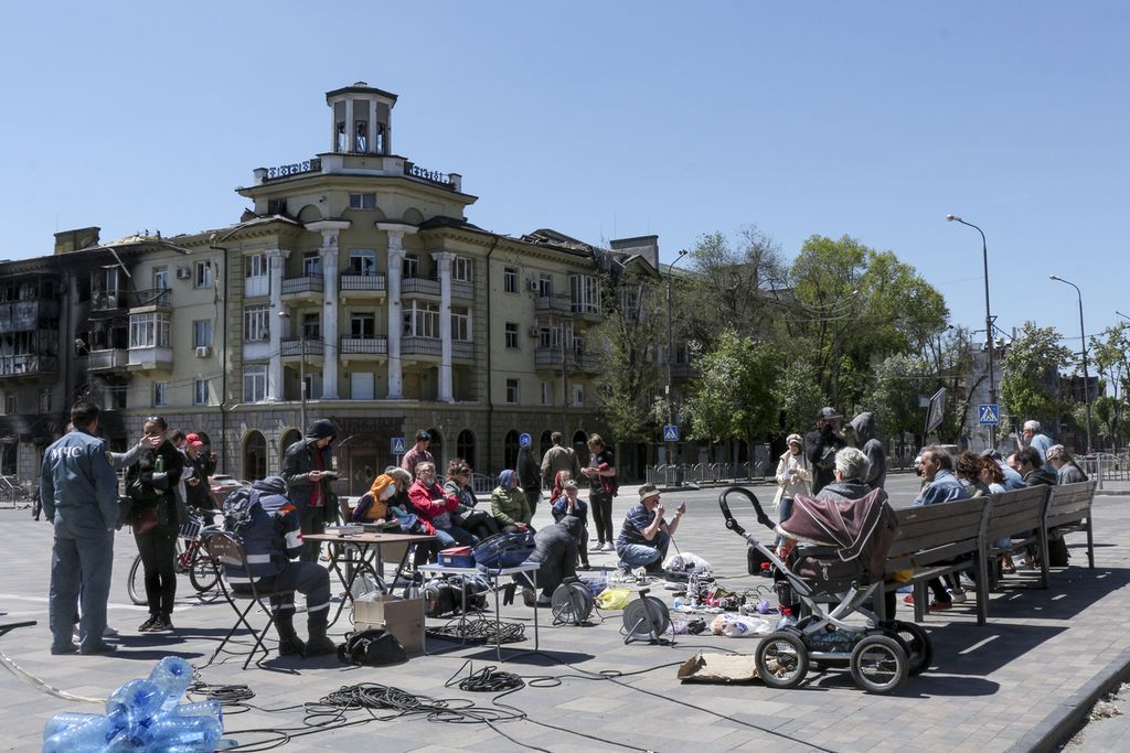 Warga berkumpul untuk mengisi daya telepon genggam mereka dari generator yang dibawa oleh Pemerintah Republik Donetsk, kelompok yang ingin memisahkan diri dari Ukraina. Foto diambil di Mariupol, Kamis (12/5/2022). (AP Photo)