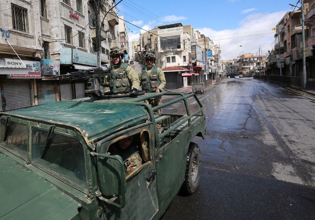 Tentara dari patroli militer Jordania berdiri di atas kendaraan militer di jalan ibu kota Amman, Jordania, selama jam malam yang diberlakukan secara nasional guna mengendalikan persebaran virus korona baru, 21 Maret 2020. 