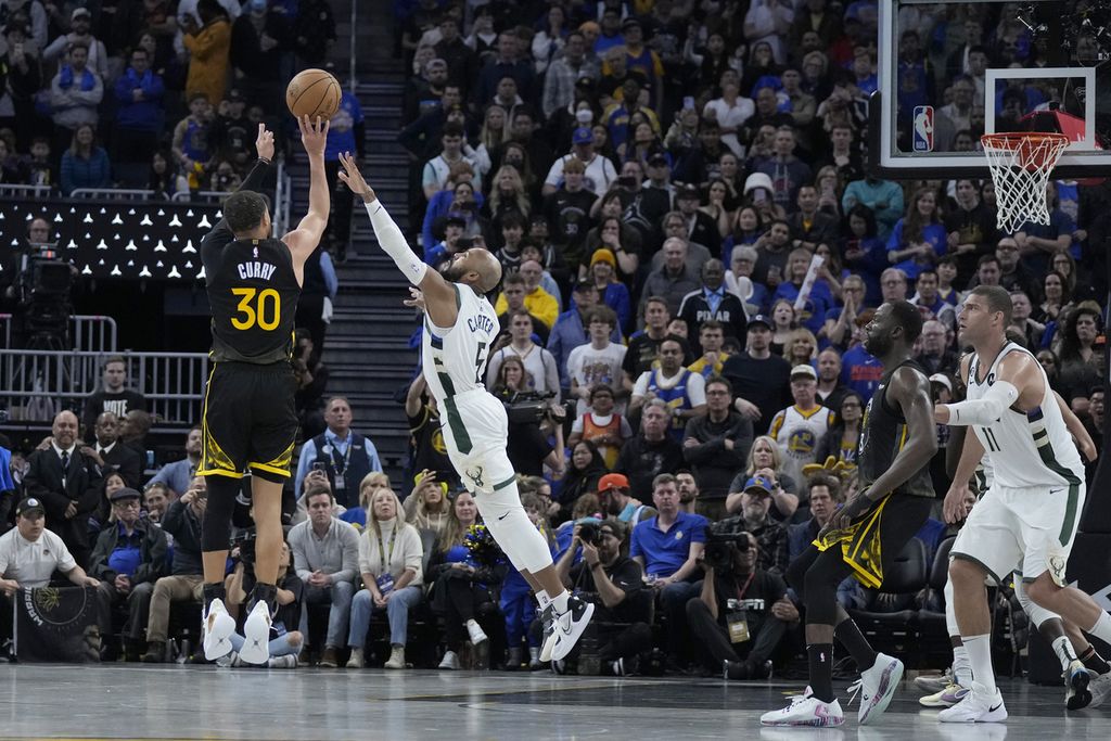 Bintang Golden State Warriors, Stephen Curry (kiri), melepaskan tembakan yang berbuah tiga poin ke keranjang Milwaukee Bucks pada laga NBA di San Francisco, Amerika Serikat, Minggu (12/3/2023) waktu Indonesia. Warriors menang, 125-116, lewat perpanjangan waktu.