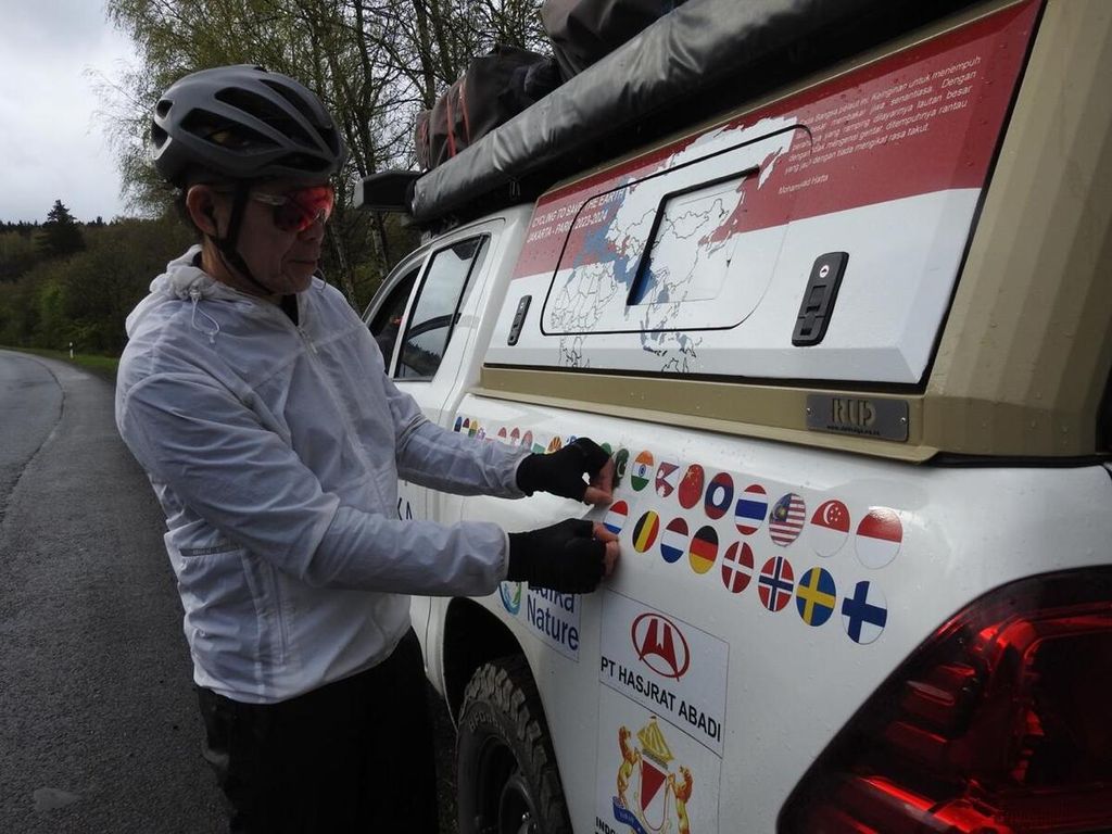 Royke Lumowa memasang stiker negara Luksemburg pada mobil pengiring di perbatasan Belgia-Luksemburg. Negara ini baru saja dimasuki setelah Belgia pada 9 April 2024.