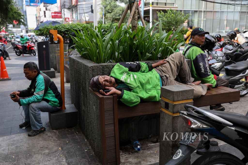 Pengemudi ojek daring tertidur saat menunggu pesanan di kawasan Dukuh Atas, Jakarta, Selasa (23/4/2024). 