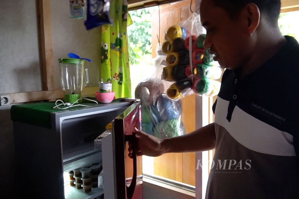 Marham Dandong (36) menunjukkan isi kulkas berisi barang dagangan, Sabtu (16/7/2022), di toko kelontong miliknya di Desa Mengkang, Bolaang Mongondow, Sulut.
