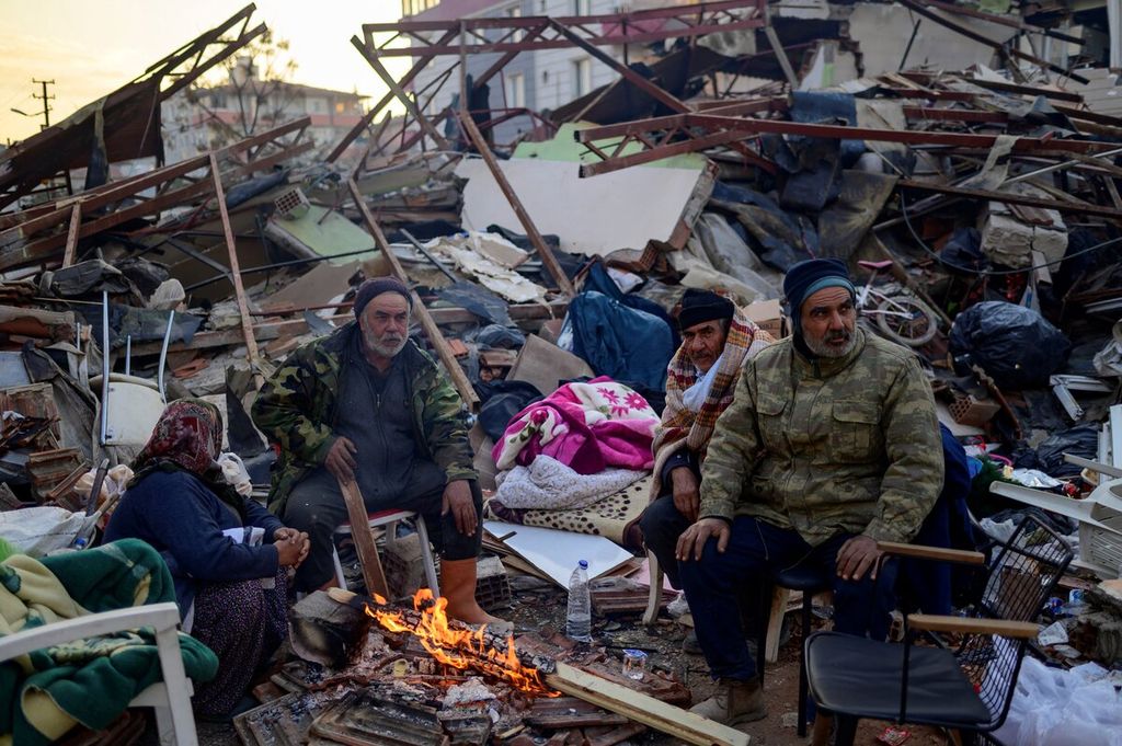 Warga berhimpun mengelilingi api unggun di antara puing-puing bangunan yang luluh lantak pascagempa bumi di Hatay, 10 Februari 2023, Jutaan warga di Turki dan Suriah kehilangan tempat tinggalnya akibat gempa yang terjadi pada Senin (6/2/2023).  