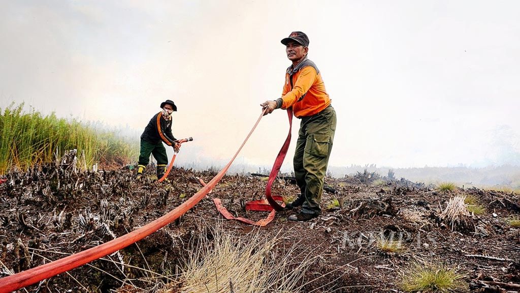 Anggota tim Manggala Agni dan Badan Nasional Penanggulangan Bencana masuk ke lahan yang terbakar dan mengatur selang untuk memadamkan api di lahan tidur seluas 15 hektar di Petuk Katimpun, Jekan Raya, Kota Palangkaraya, Kalimantan Tengah, Minggu (19/8/2018). 