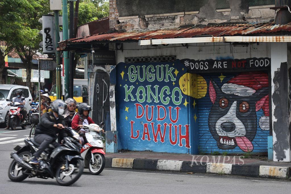 Warga melintas di depan mural tentang ajakan menghentikan praktik konsumsi daging anjing di Simpang Wirobrajan, Yogyakarta, Senin (20/2/2023).