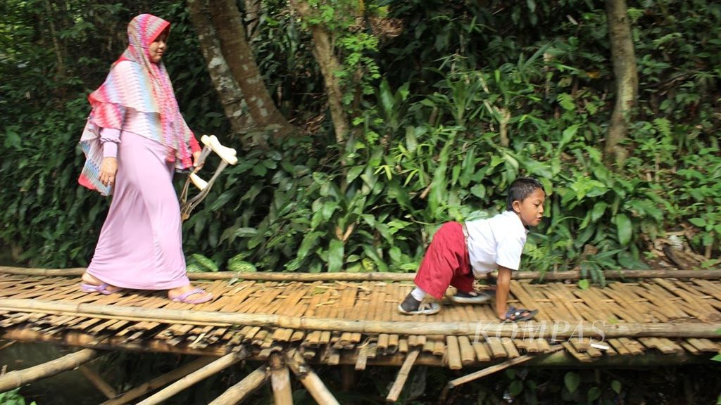 Muklis Abdul Kholik (8), siswa kelas III SD Negeri 10 Cibadak, Kabupaten Sukabumi, Jawa Barat, merangkak melewati jembatan bambu menuju rumahnya di Kampung Cikuwul Tonggoh, Cibadak, Senin, (12/11/2018). Siswa disabilitas itu tetap bersemangat ke sekolah meskipun harus merangkak sejauh sekitar 3 kilometer.