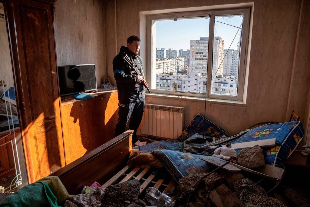Seorang polisi melihat melalui jendela sebuah flat yang rusak di sebuah kawasan permukiman warga yang terkena puing-puing dari roket yang jatuh di Kiev, Kamis (17/3/2022). 