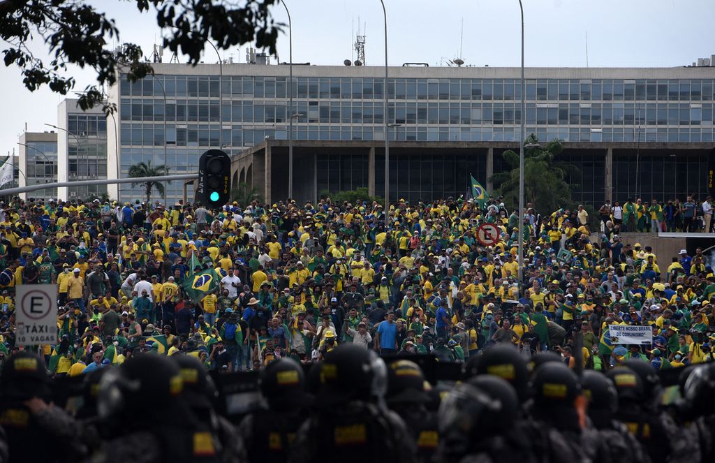 Pendukung mantan Presiden Brasil Jair Bolsonaro yang menyerang beberapa gedung pemerintah dihadang pasukan keamanan (latar depan) di Brasilia, Minggu (8/1/2023). Ribuan pendukung mantan presiden sayap kanan Brasil Jair Bolsonaro menerobos barikade polisi dan menyerbu kongres, istana presiden, dan mahkamah agung. 