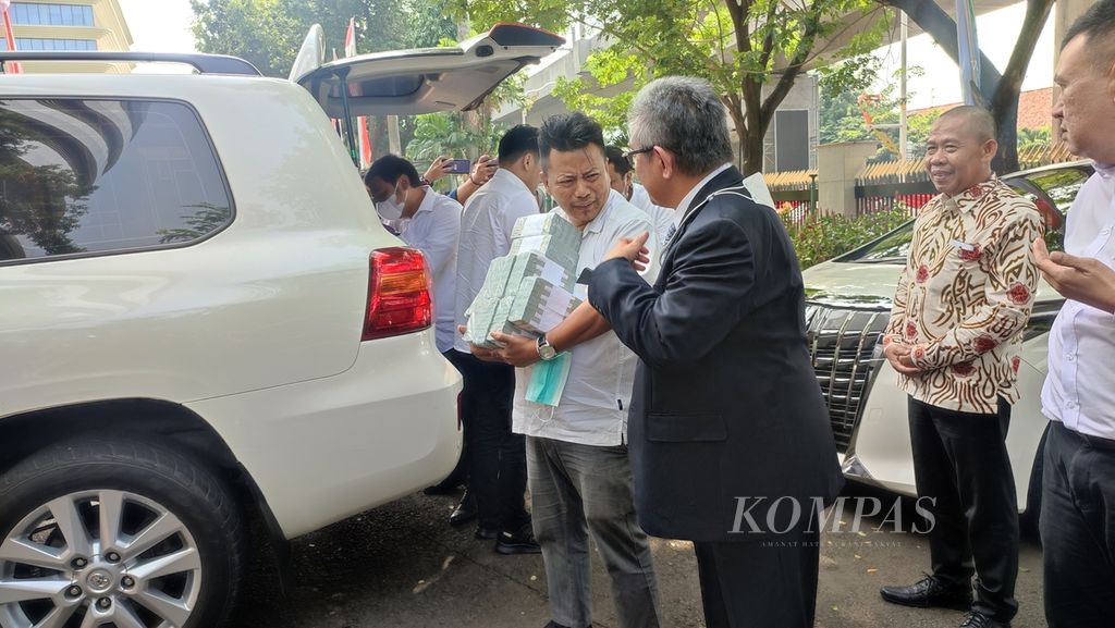 Advokat Handika Honggowongso (kiri) membawa uang dalam pecahan dollar AS bersama advokat Maqdir Ismail (memakai jas) ketika tiba di Kejaksaan Agung, Jakarta, Kamis (13/7/2023).