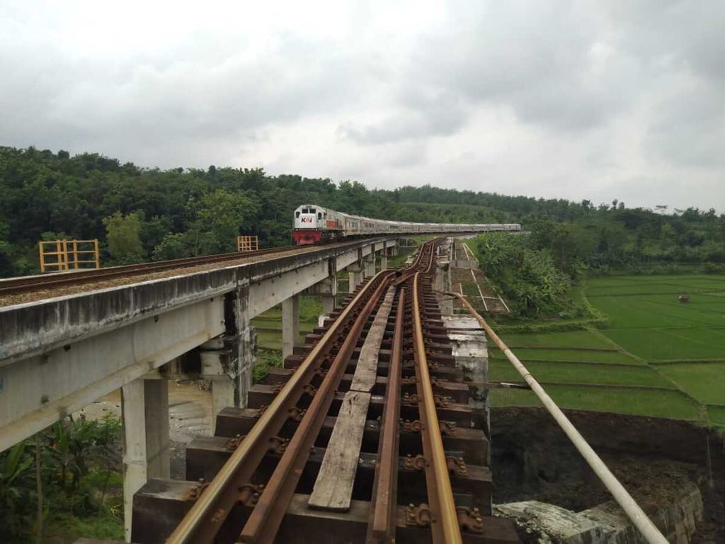 Kereta api melintas dengan kecepatan 20 kilometer per jam di salah satu jembatan di Desa Tonjong, Brebes, Jawa Tengah, Selasa (12/1/2021) siang. Kereta hanya bisa melintas di satu jalur karena jembatan di sebelahnya (kanan) ambrol akibat tergerus aliran sungai.