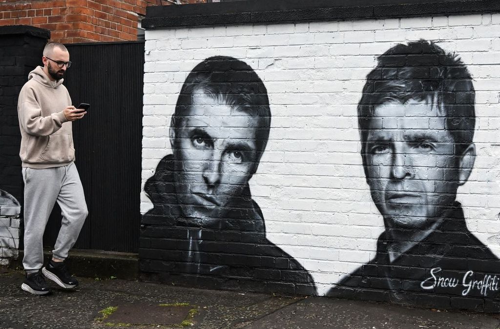 Seorang pejalan kaki berjalan melewati mural yang dibuat oleh seniman Scott Wilcock alias Snow Graffiti, yang menggambarkan Liam Gallagher (kiri) dan Noel Gallagher, anggota band rock Inggris, Oasis, dan dilukis di luar pub Whitefield, Manchester, Inggris, pada 2 September 2024.