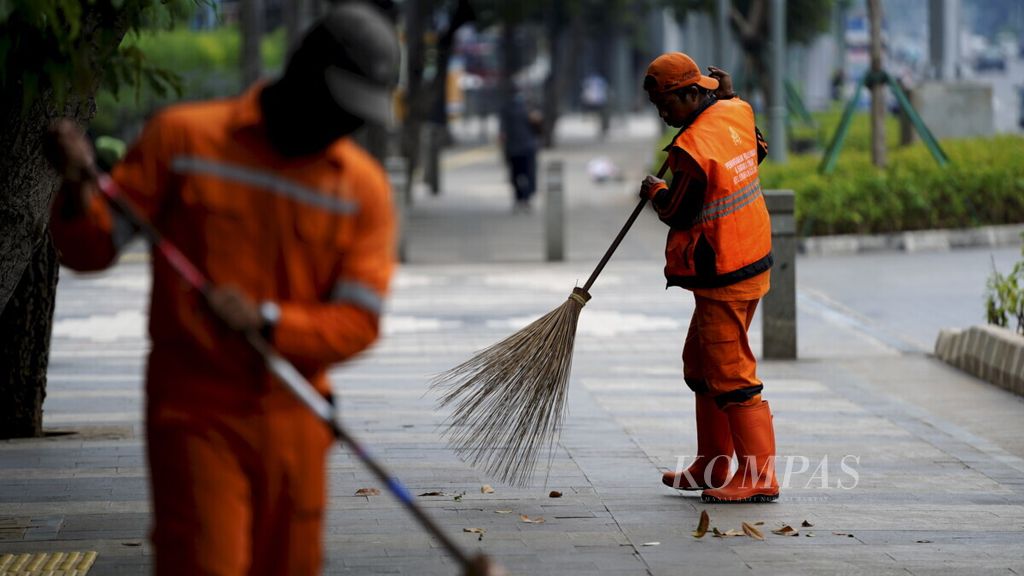 Petugas kebersihan menggunakan masker menyapu Jalan Sudirman, Jakarta Selatan, Jumat (27/3/2020). Kebersihan Ibu Kota tetap terjaga di tangan mereka di tengah merebaknya Covid-19.