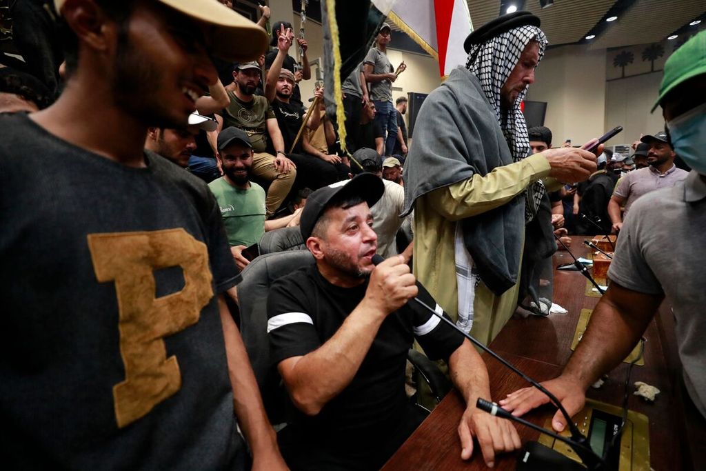 Seorang pria menggunakan mikrofon di meja anggota parlemen dalam aksi pendudukan gedung parlemen oleh para pendukung ulama Irak, Moqtada al-Sadr, di Baghdad, Irak, Sabtu (30/7/2022). 