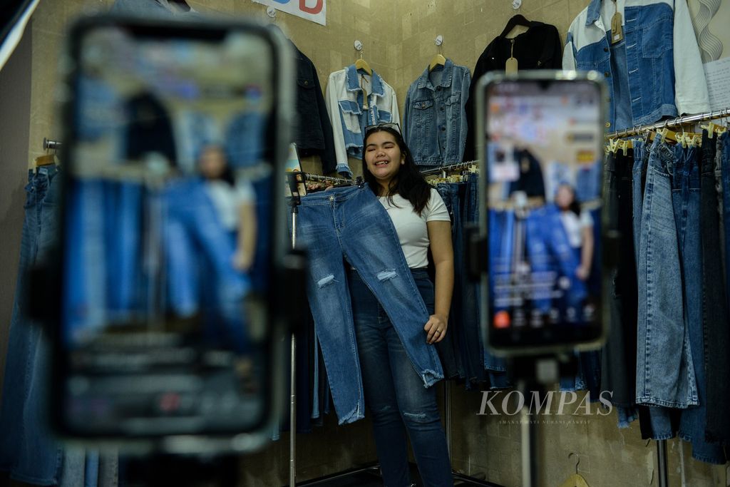 Pedagang menawarkan celana kepada pengguna media sosial Tiktok saat siaran langsung di kios Blok B Tanah Abang, Jakarta, Selasa (13/6/2023). Penjualan secara daring menjadi salah satu strategi para pedagang untuk menjangkau konsumen yang lebih luas. 