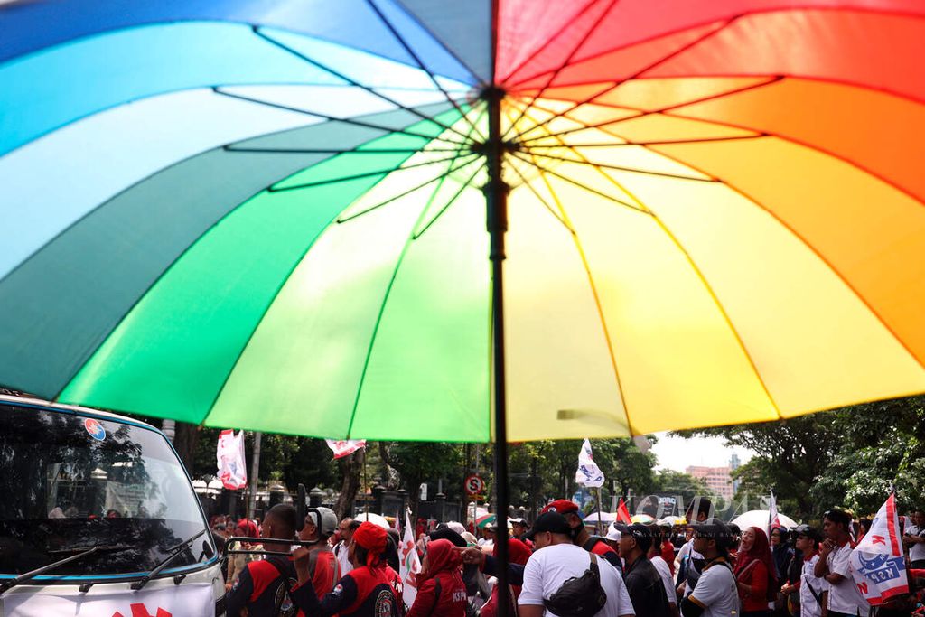 A vendor's umbrella with a background of a protest to commemorate Labor Day on Pahlawan Street, Semarang City, Central Java, on Wednesday (1/5/2024). The workers who were on holiday still carried out a solidarity action for labor rights, demanding their welfare and pushing for government policy changes related to several laws that are not in their favor.