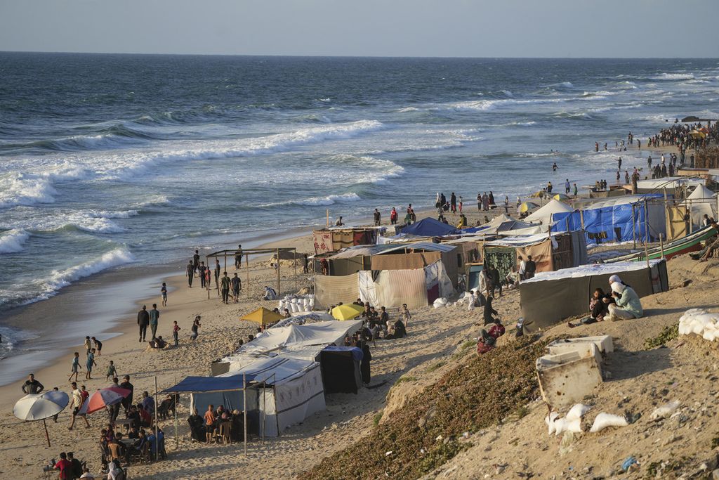 Warga Palestina yang mengungsi akibat serangan udara dan darat Israel di Jalur Gaza berjalan di sepanjang pantai Laut Mediterania di kamp tenda darurat di Deir al Balah pada 13 Mei 2024. 