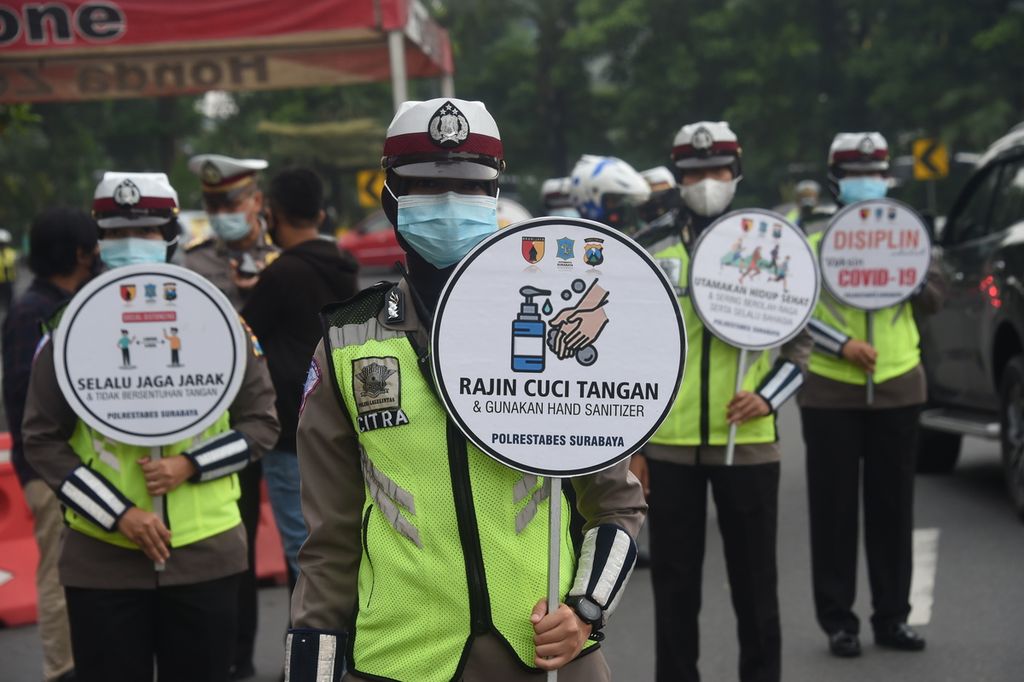 Petugas membawa poster saat berlangsung sosialisasi oleh petugas gabungan pada hari pertama pemberlakuan pembatasan kegiatan masyarakat (PPKM) di Bundaran Waru, Surabaya, Jawa Timur, Senin (11/1/2021). 