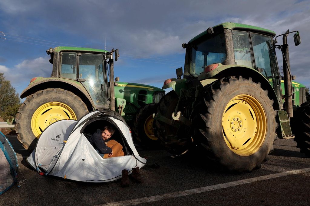 Seorang petani keluar dari tendanya saat ia dan petani lainnya memblokade Jalan Tol AP7, penghubung Spanyol-Perancis, dengan traktor-traktor dalam unjuk rasa di Pontos, dekat Figueras, wilayah Catalonia, Spanyol, sekitar 40 kilometer dari perbatasan dengan Perancis, 27 Februari 2024. 