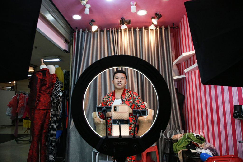 Uger Situmeang, karyawan di gerai pakaian Klementine di Mal Ambasador, Jakarta Selatan, menawarkan produk pakaian melalui siaran langsung di media sosial, Rabu (13/7/2022). 