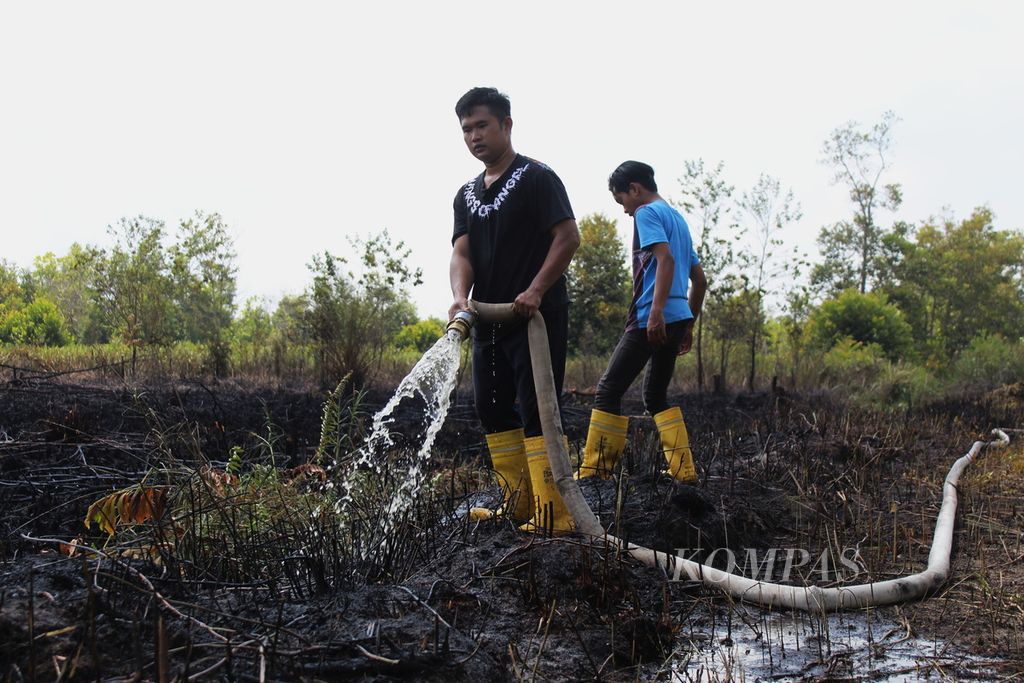 Petugas pemadam kebakaran hutan dan lahan melakukan pembasahan lahan yang baru terbakar di Jalan Kalibata, Kota Palangkaraya, Kalimantan Tengah, Senin (14/8/2023).