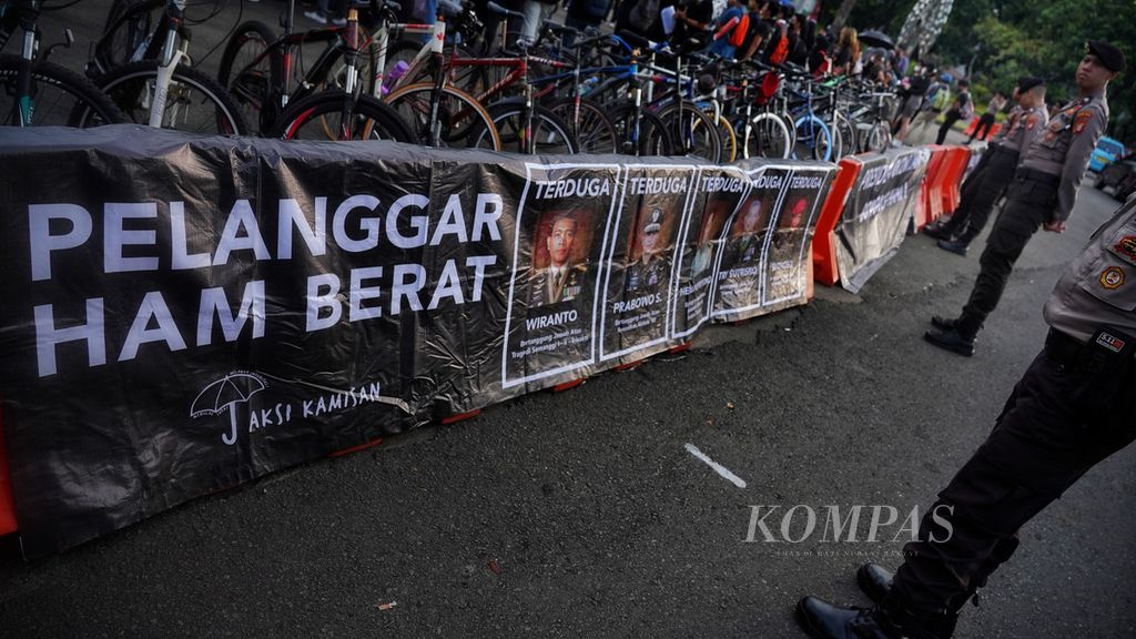 Polisi menghadap poster yang dibentang aktivis Kamisan bersama mahasiswa Sekolah Tinggi Filsafat Driyarkara saat menggelar Aksi Kamisan Ke-772 di depan Istana Merdeka, Jakarta, Kamis (4/5/2023).