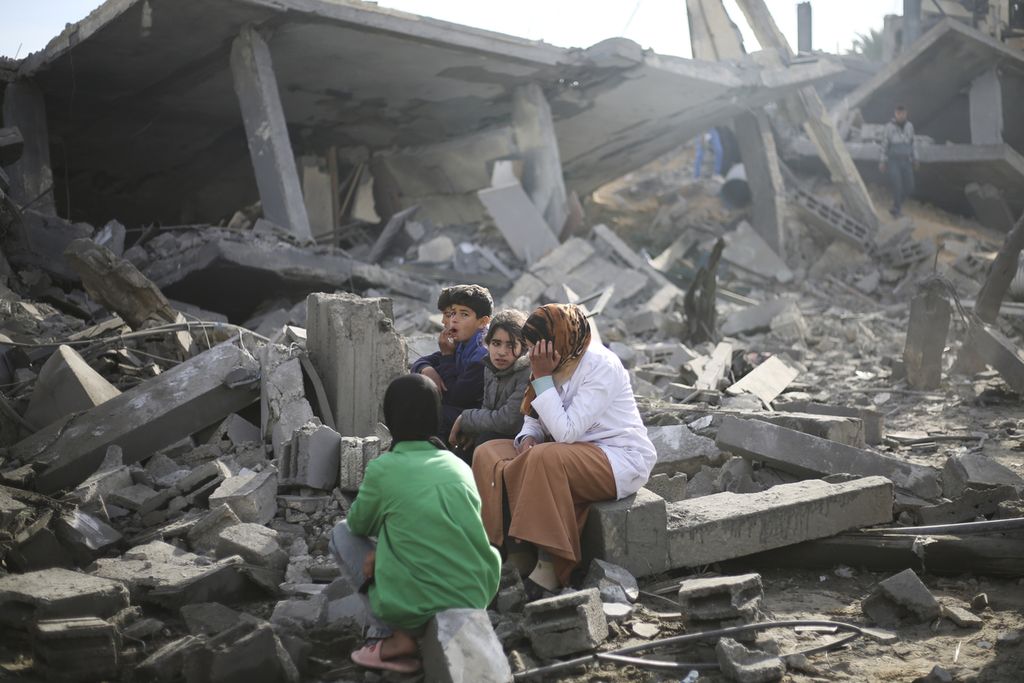 Warga Palestina duduk di puing-puing gedung di Rafah, Jalur Gaza, pada 12 Februari 2024.   