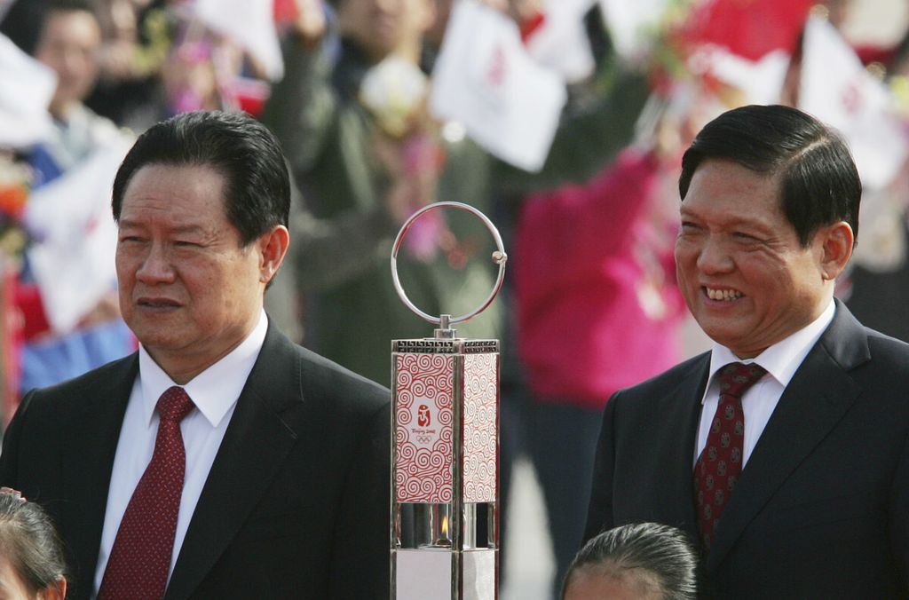 Dalam foto yang diambil pada 31 Maret 2008 ini, anggota Komite Tetap Politbiro Partai Komunis China Zhou Yongkang (kiri) dan Presiden Olimpiade Beijing Liu Qi (kanan) menunggu kedatangan api olimpiade di Bandara Beijing. Tahun 2014, Zhou Yongkang diadili dengan dakwaan terlibat kasus korupsi dan suap. Zhou dihukum seumur hidup. 