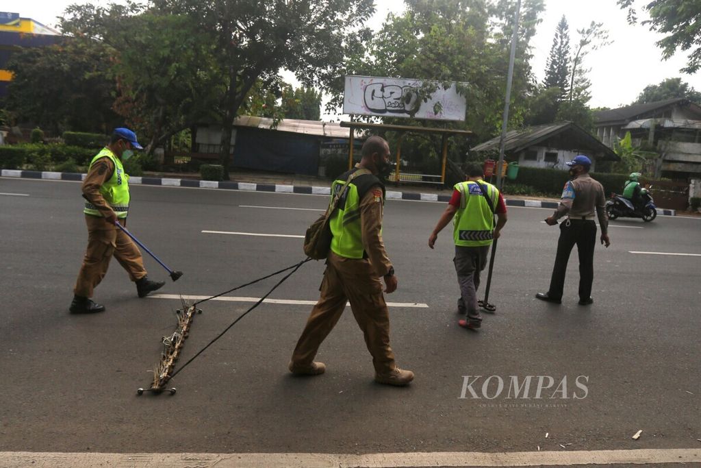 Komunitas saber ranjau paku bersama Satlantas Jakarta Barat, dengan menggunakan magnet, membersihkan Jalan Letjen S Parman, Tomang, Jakarta, dari ranjau paku yang sengaja disebar oleh oknum tidak bertanggung jawab, Minggu (9/3/2021). 