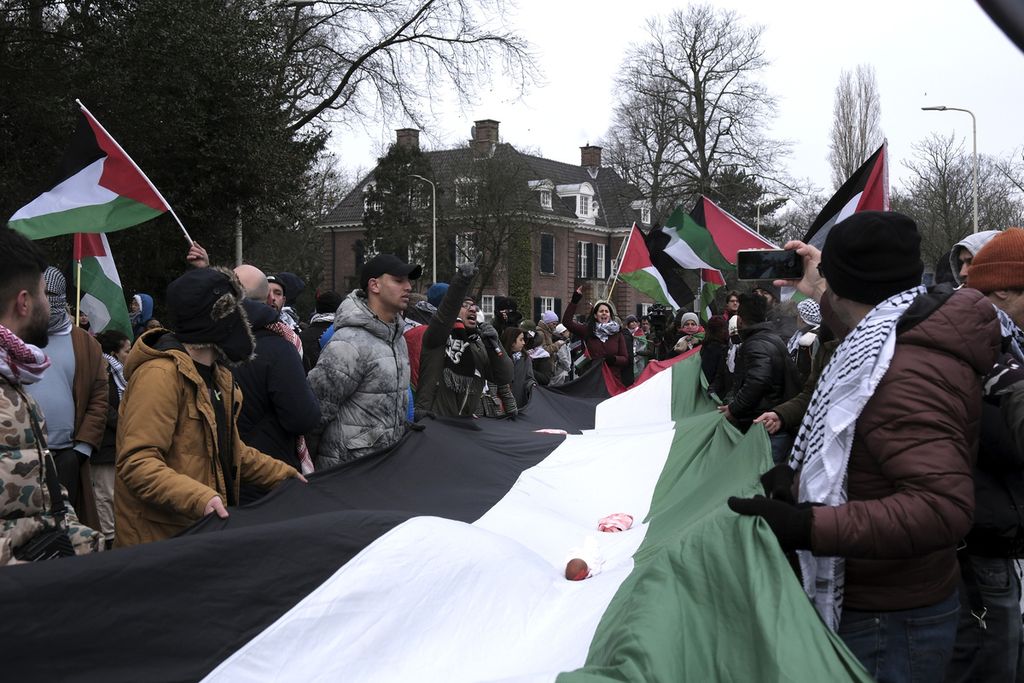 Para pengunjuk rasa membawa bendera raksasa Palestina, dengan boneka yang dibungkus untuk mewakili anak-anak yang tewas dan terluka, selama demonstrasi di luar Mahkamah Internasional di Den Haag, Belanda, Kamis (11/1/2024).